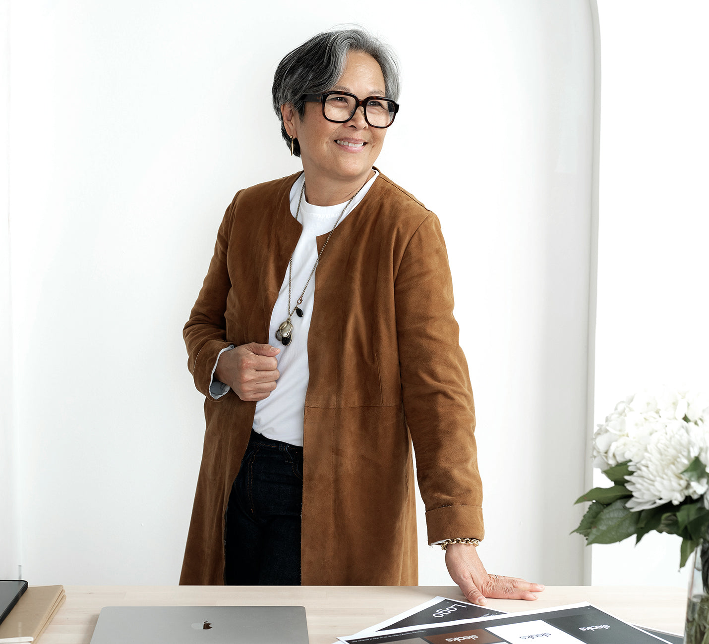 kathy vurinaris Owner of the store wearing a brown coat standing in an office setting with a white wall and desk